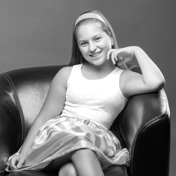 Beautiful teen girl sits in the studio on a leather chair. Concept of youth fashion and culture.