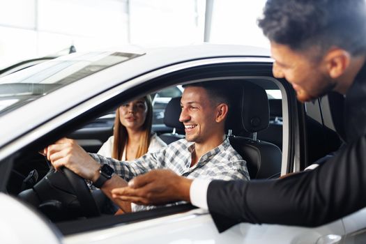 Young couple choosing a car at the dealership with manager helping them