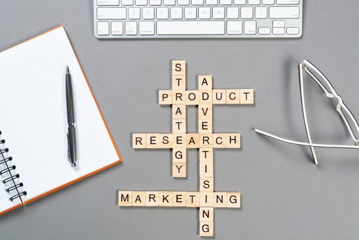 Web marketing concept with words from cubes. Still life of office workplace with crossword. Flat lay grey surface with computer keyboard and notebook. Sales strategy planning and product promotion.