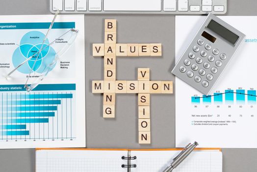 Brand value concept with words from cubes. Still life of office workplace with crossword. Flat lay grey surface with computer keyboard and calculator. Strategy planning and business management.