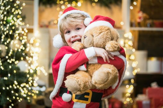 Santa helper. Surprised Little Santa boy in embrace teddy bear