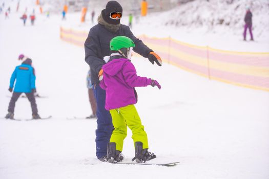 At Cold Winder Day at Mountain Ski Resort Father Teaching Little Daughter Snowboarding