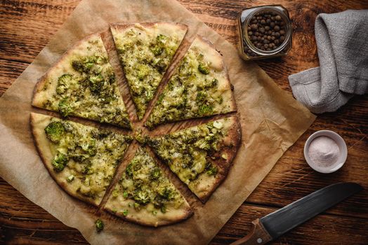 Sliced homemade pizza with broccoli, pesto sauce, herbs and cheese on baking paper. View from above