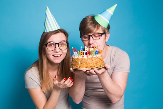 Young cheerful students charming girl and nice guy in greeting paper caps holding a cake with a bengal sparks candle. Concept of congratulations on the holiday and anniversary