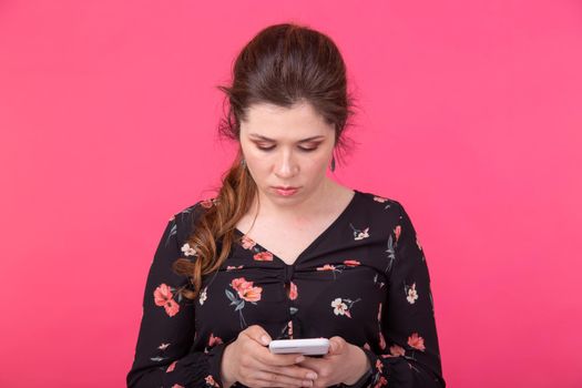 Communication and technologies concept - Portrait of a woman sending text message from her phone on pink background.