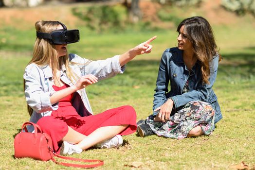Two women looking in VR glasses and gesturing with his hands outdoors in urban park