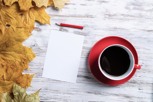 Flat lay autumn composition with cup of black tea and yellow autumn leaves. Time of tea break concept. Hot drink and blank paper sheet with pen lies on vintage wooden desk with bright foliage.