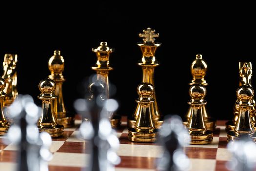 Gold and silver chess figures standing on chessboard. Intellectual and tactic game. Strategy planning, leadership and teamwork business concept. Close-up metal chess pieces on black background.