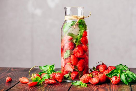 Bottle of Detox Water Infused with Fresh Strawberry and Basil Leaves. Scattered Ingredients on Wooden Table. Copy Space.