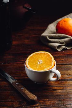 Half of orange in a white cup over rustic table