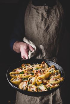Chef holds skillet of baked jumbo shells pasta stuffed with ground beef, spinach and cheese