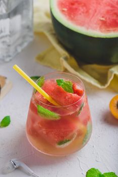 Fresh watermelon cocktail with gin and sparkling water, garnished with mint leaves and yellow straw in glass on light concrete background.
