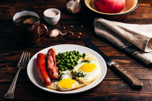 Breakfast with fried eggs, sausages and green peas on white plate