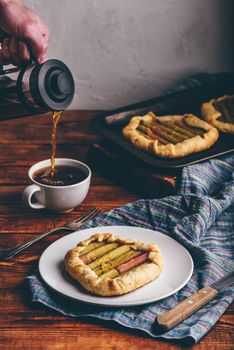 Rhubarb mini galette on white plate. Hand with french press pouring coffee