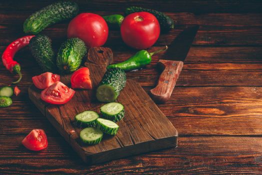 Sliced vegetables. Tomatoes, cucumbers and chili peppers over wooden background.