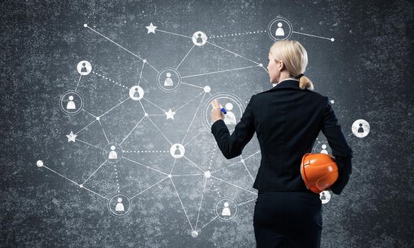 Businesswoman pointing on abstract social network. Back view of woman headhunter in business suit and safety helmet. Social connection structure. Human resources recruitment and people networking.