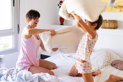 Mother and daughter having funny pillow fight on bed. Mum spending free time with her daughter.