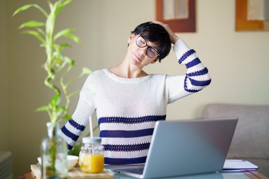 Woman teleworking from home with her laptop taking a stretch break.