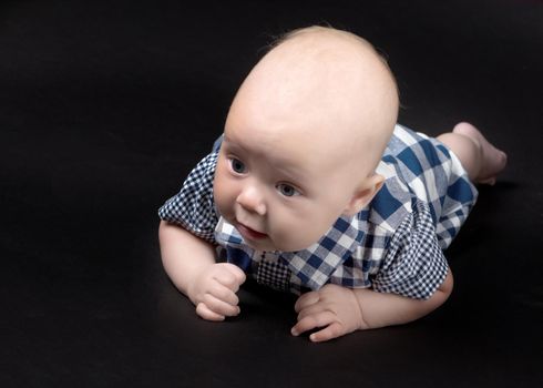 A charming baby lies on the blanket and looks into the camera on a black background. The concept of a happy childhood, the birth and upbringing of a child.