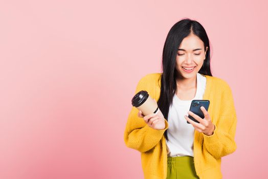 Happy Asian portrait beautiful cute young woman excited smiling holding mobile phone and coffee to go, studio shot isolated on pink background, female using smartphone with coffee cup take away