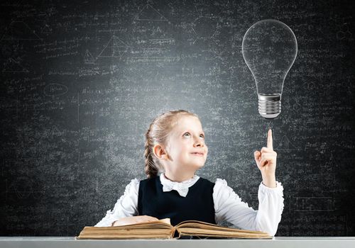 Little girl scientist with microscope on chalkboard background with light bulb. Research and discovery concept. Elementary science class in modern school. Schoolgirl in schoolwear sitting at desk