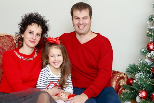 Happy parents with little daughter in a relaxed family atmosphere in the New year.Around the Christmas tree.