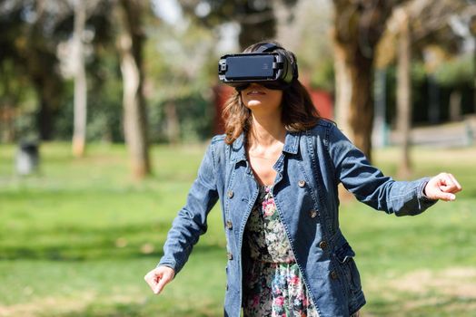 Woman looking in VR glasses and gesturing with his hands outdoors in urban park.
