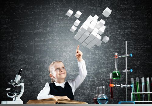 Little girl scientist with microscope on chalkboard background. Research and discovery. Elementary science class in school. Schoolgirl in schoolwear sits at desk and finger pointing on 3d cubes