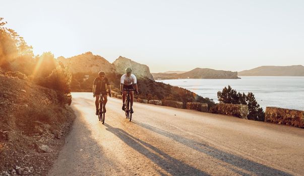 Two professional male cyclists riding their racing bicycles in the morning together on coastal road