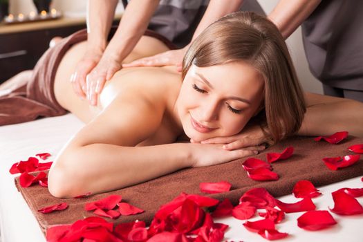 Young woman having massage in beauty spa by two therapist
