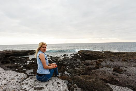 Women on volcanic rocks and blue ocean with waves, white foam and volcanic rocks. Canary Islands. The magnificent coast of the Atlantic Ocean.