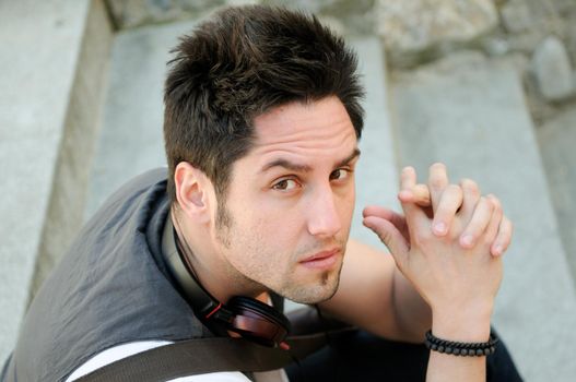 Portrait of young serious man sitting on steps, with headphones