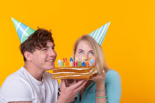 Young cheerful students charming girl and nice guy in greeting paper caps holding a cake with a bengal sparks candle. Concept of congratulations on the holiday and anniversary