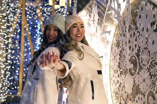 Two girlfriends asian girls in white coats are having fun hugging, new year, light bulbs