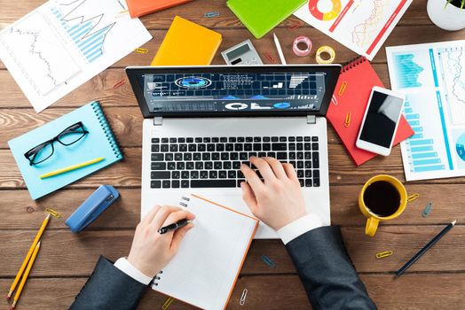 Close up businessman hands working at laptop. Top view office workplace with computer and financial documents on wooden table. Business occupation design with man in business suit sitting at desk