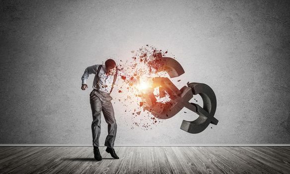 Young furious businessman in empty room crashing with fist stone dollar symbol