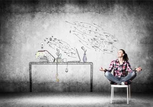 Young happy woman relaxing in room. Creative freelancer sitting in lotus pose on chair. Home workspace with computer on desk illustration on wall. Smiling girl doing yoga at home in leisure time.