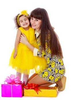 Slender young mother in a short elegant dress and her cute little daughter , embracing, surrounded by Christmas gifts.Isolated on white background.