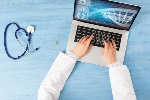 Top view of doctor hands typing at laptop computer. Therapist in white coat sitting at blue wooden desk. Online medical clinic communication with patient. Medical application and healthcare services.
