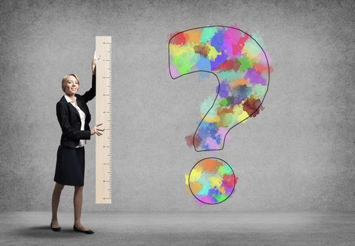 Woman holding big ruler on wall background. Businesswoman measuring question mark with ruler. Human resources recruitment. Creative motivation, coaching and mentoring. Testing and examination concept.