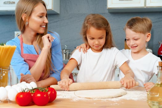 Mother and her little kids, boy and girl, helping her to prepare dough close up