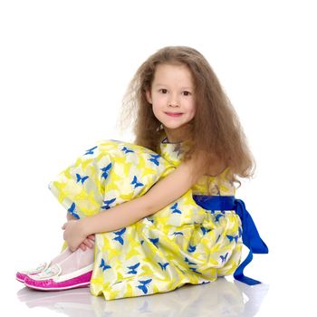 Beautiful little girl is sitting on the floor in the studio. The concept of a happy childhood, beauty and fashion. Isolated on white background.