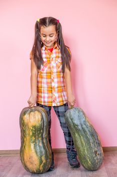 Picture of cheerful positive little girl with pumpkin over pink wall background holding pumpkin showing peace.