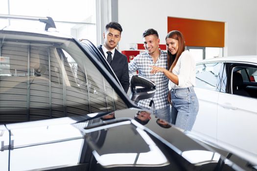 Young couple choosing a car at the dealership with manager helping them