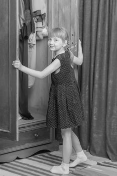 A nice little girl looks in the old wardrobe wardrobe. The concept of fashion, retro style, things of the fifties of last century.