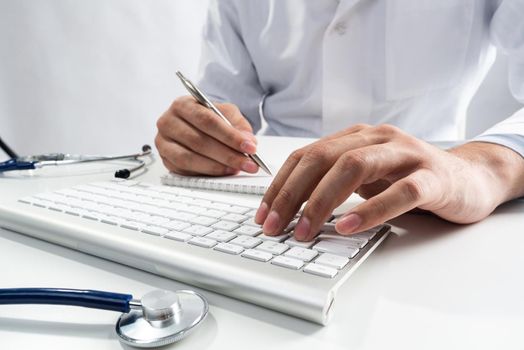 Doctor typing on wireless computer keyboard in office. Physician in white medical gown works with computer at desk. Professional diagnosis and treatment in modern hospital. Professional healthcare