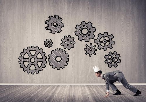 Young handsome businessman wearing white paper crown running and gear mechanism on wall