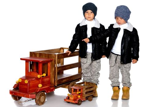 Two little boys play with wooden cars. In autumn jackets and hats. Isolated on white background.