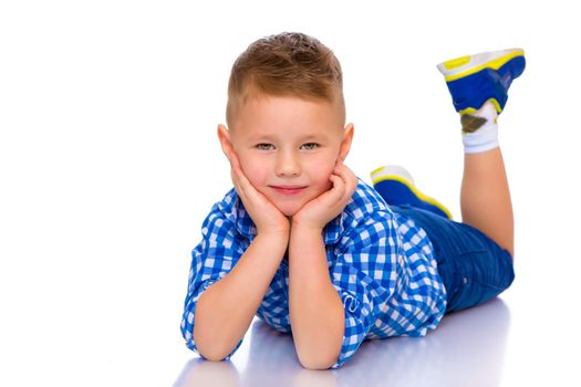 Happy little boy lies on the floor in the studio on a white background. The concept of a happy childhood, rest and vacation. Isolated.