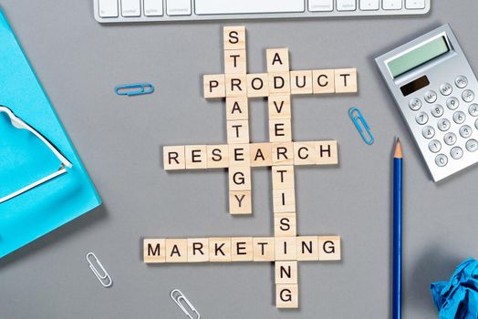 Web marketing concept with words from cubes. Still life of office workplace with crossword. Flat lay grey surface with computer keyboard and notebook. Sales strategy planning and product promotion.